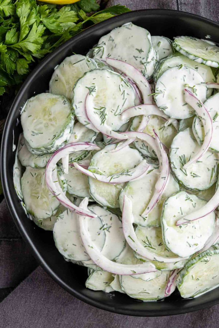 A bowl of creamy cucumber salad with sliced cucumbers, red onions, and a rich dill dressing.