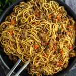 A pan filled with cooked noodles, ground meat, and diced red bell peppers captures the essence of viral Dirty Spaghetti, with metal tongs resting inside.