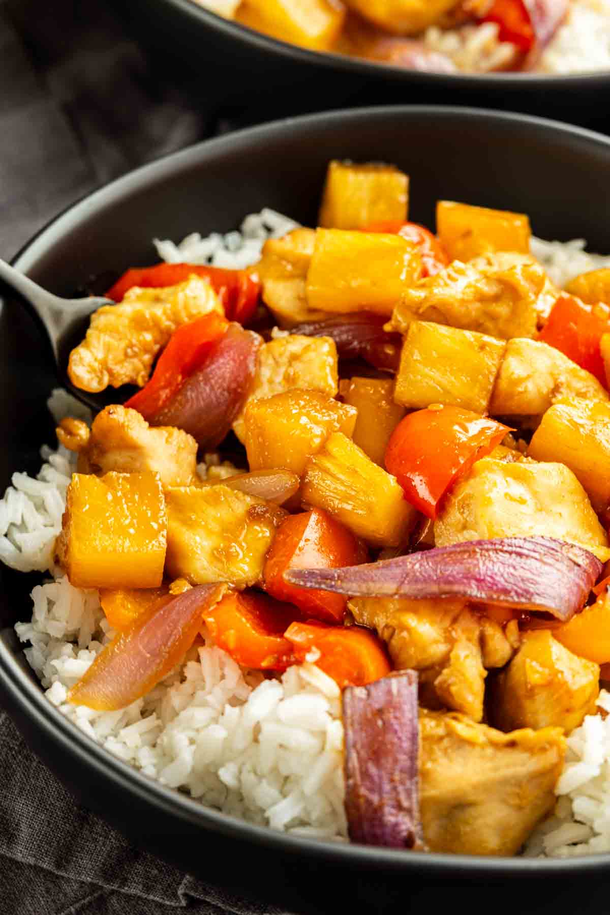 A bowl of white rice topped with stir-fried chicken, pineapple chunks, red bell peppers, carrots, and red onions—perfect for an easy weeknight dinner.