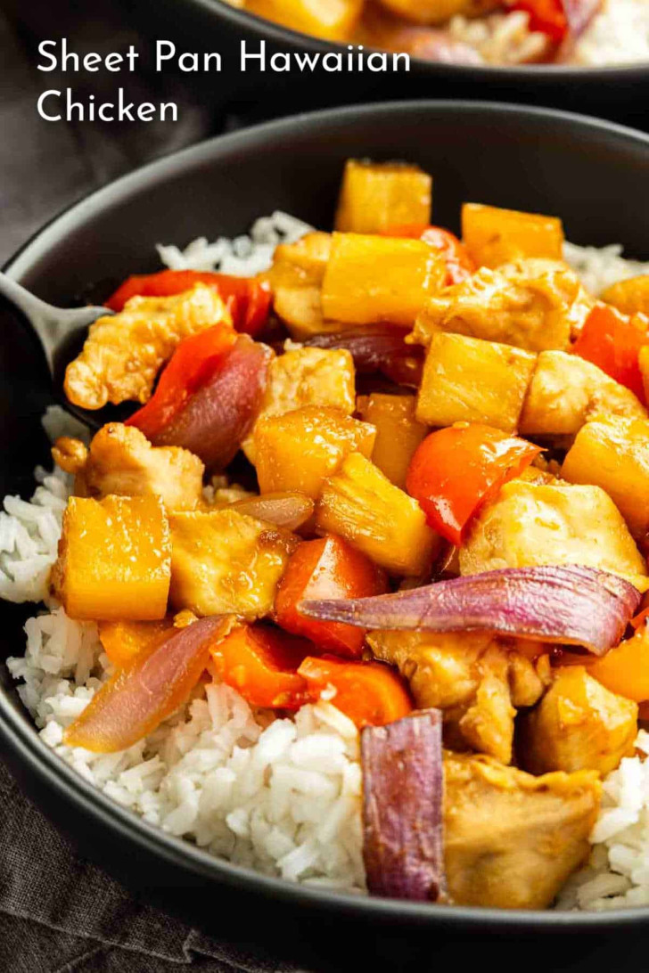 A black bowl filled with white rice, topped with pieces of chicken, pineapple chunks, red onion, and carrots. Text in the corner reads "Sheet Pan Hawaiian Chicken.