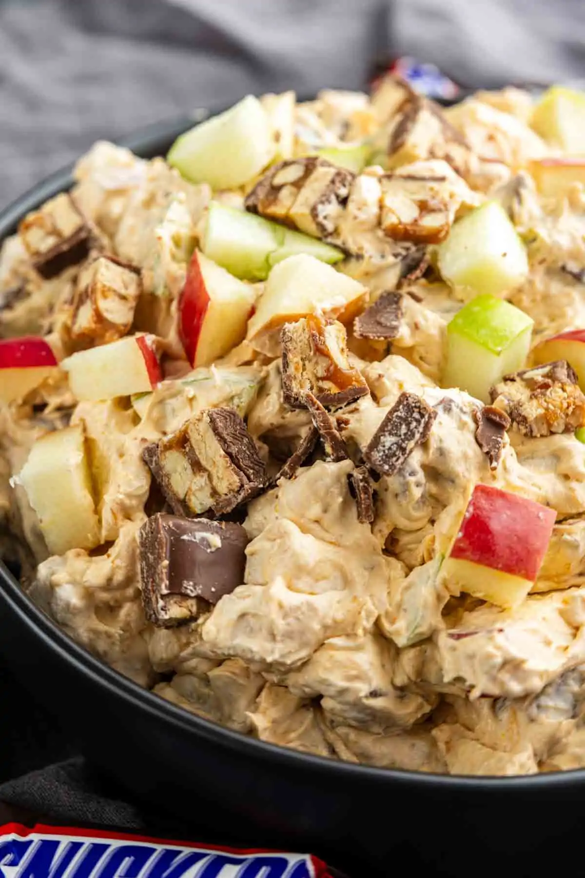 A bowl of creamy Snickers Salad mixed with chopped apples and pieces of chocolate candy bars.