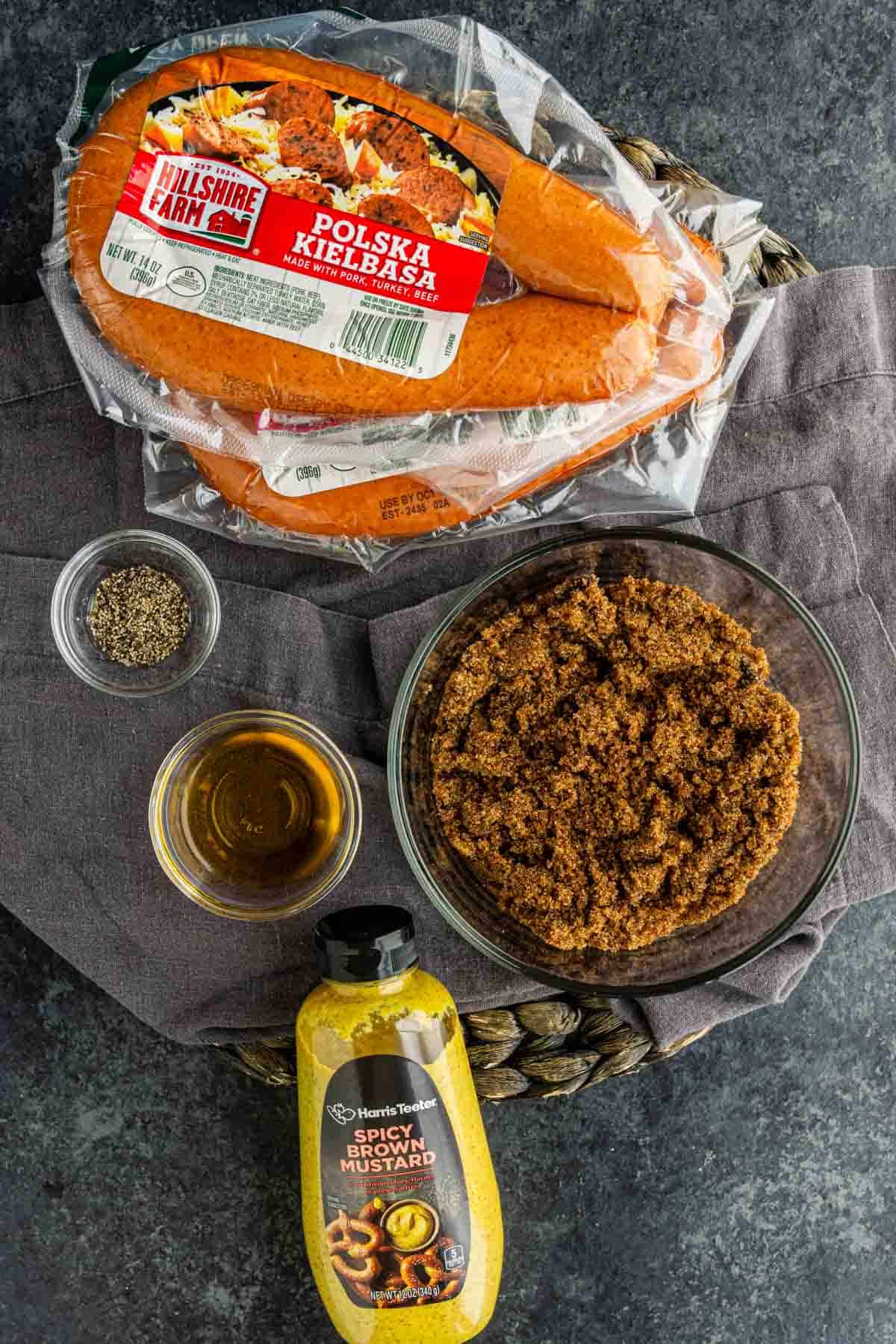 A package of Polska kielbasa, brown sugar, spicy brown mustard, black pepper, and honey on a gray cloth—perfect ingredients for a flavorful BBQ kielbasa bites or your next favorite kielbasa appetizer recipe.