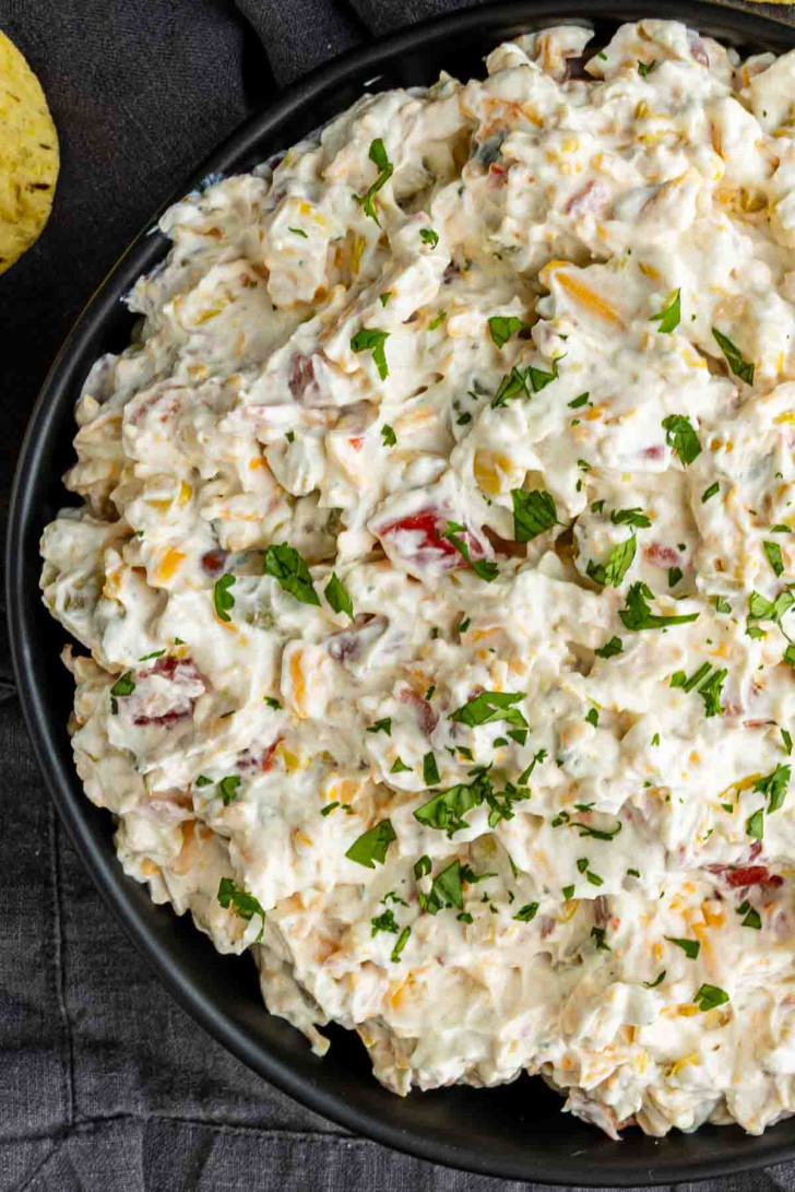 A close-up of a bowl filled with creamy potato salad garnished with chopped parsley.