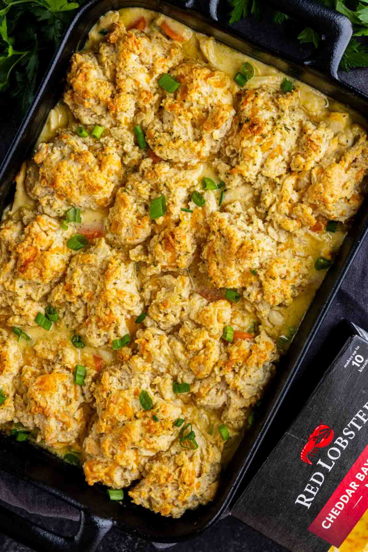 A baked Cheddar Bay Biscuit Chicken Casserole topped with golden-brown biscuit pieces and garnished with chopped green onions, served beside a box of Red Lobster Cheddar Bay Biscuit Mix.