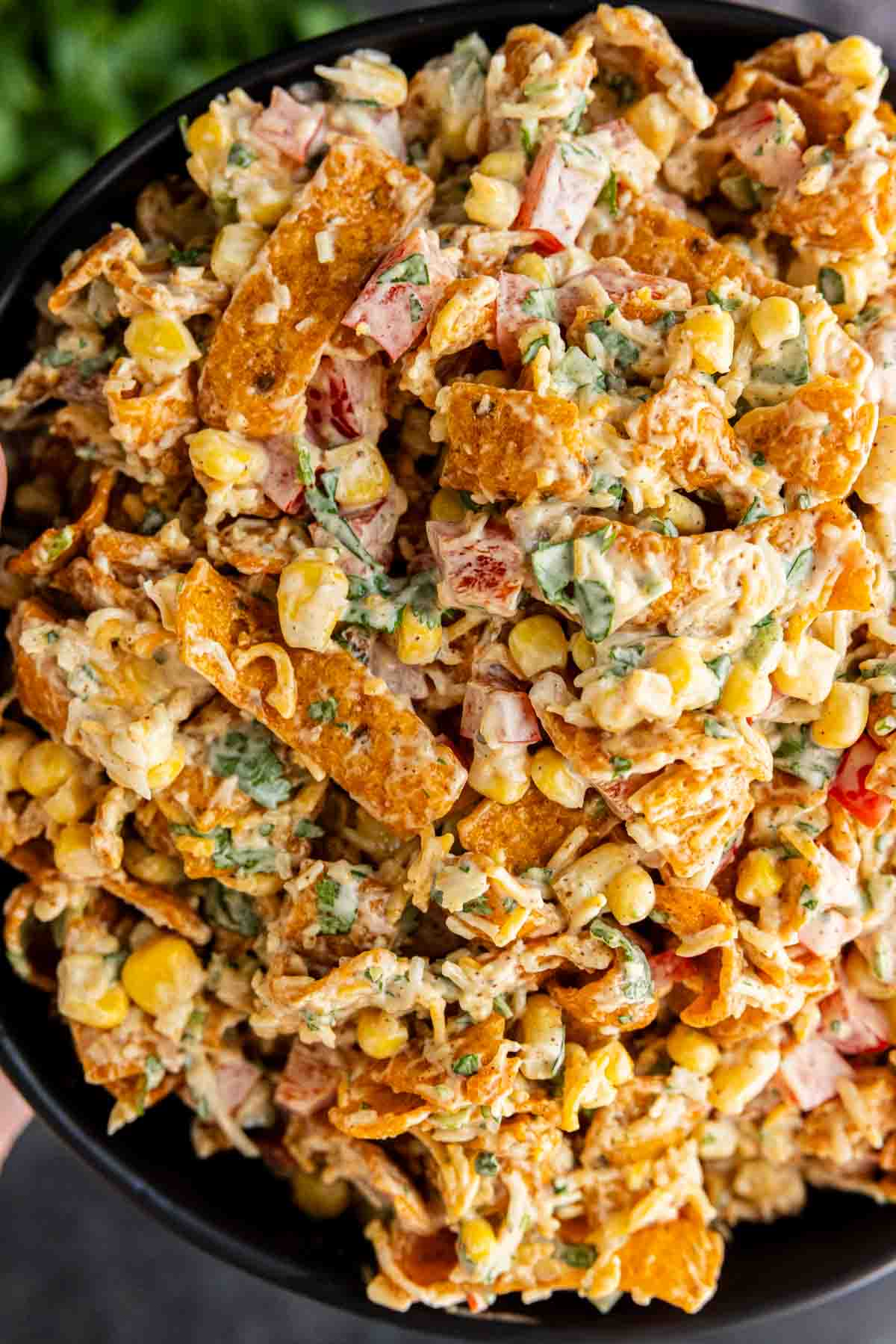 A close-up of a bowl filled with creamy Frito Corn Salad, mixed with chopped vegetables, shredded cheese, and crunchy Fritos chips.