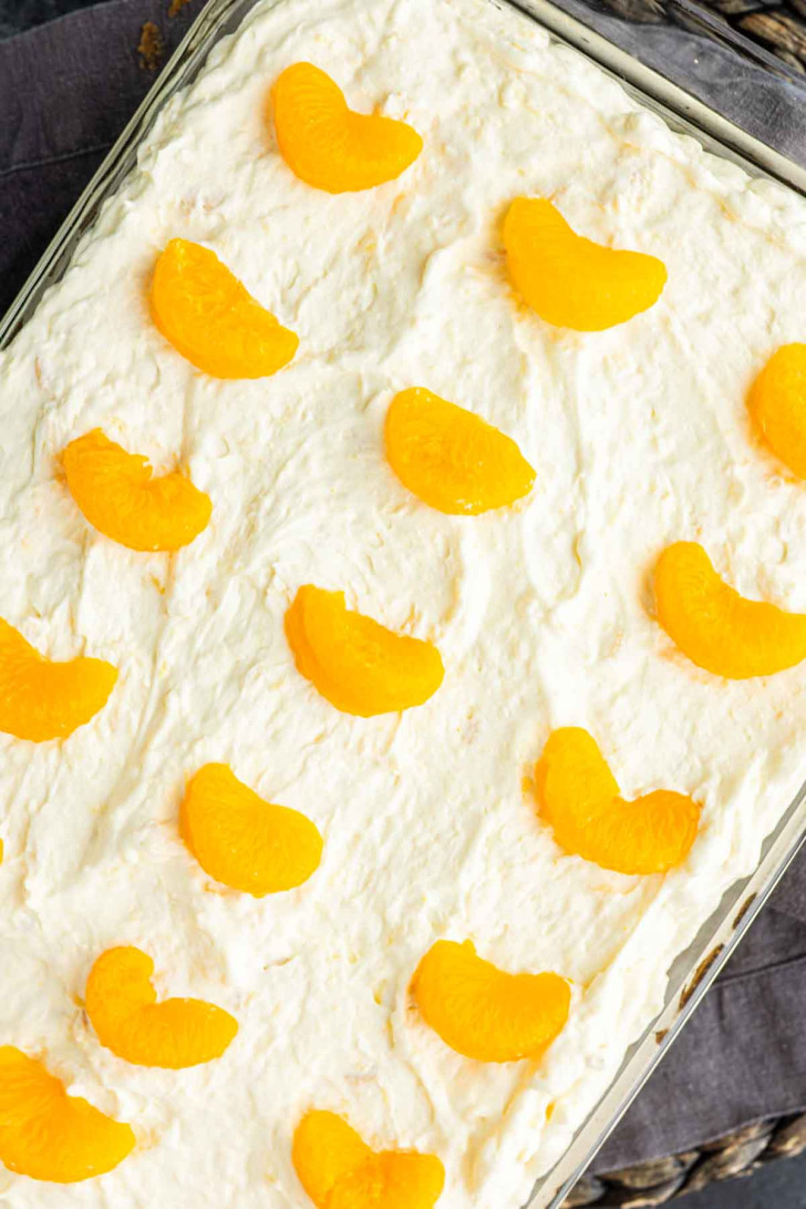 A rectangular dish filled with a creamy dessert is topped with evenly spaced mandarin orange segments.