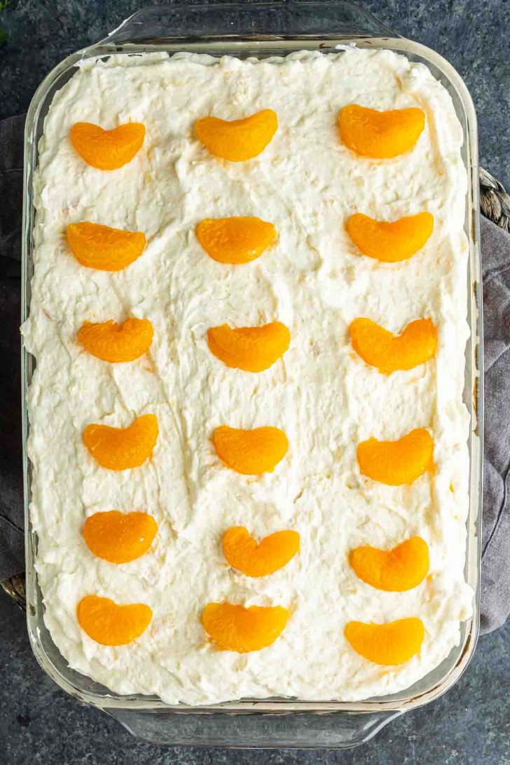 Rectangular glass dish filled with a creamy mandarin orange cake, topped with evenly spaced mandarin segments in rows for a classic Pig Pickin’ Cake presentation.