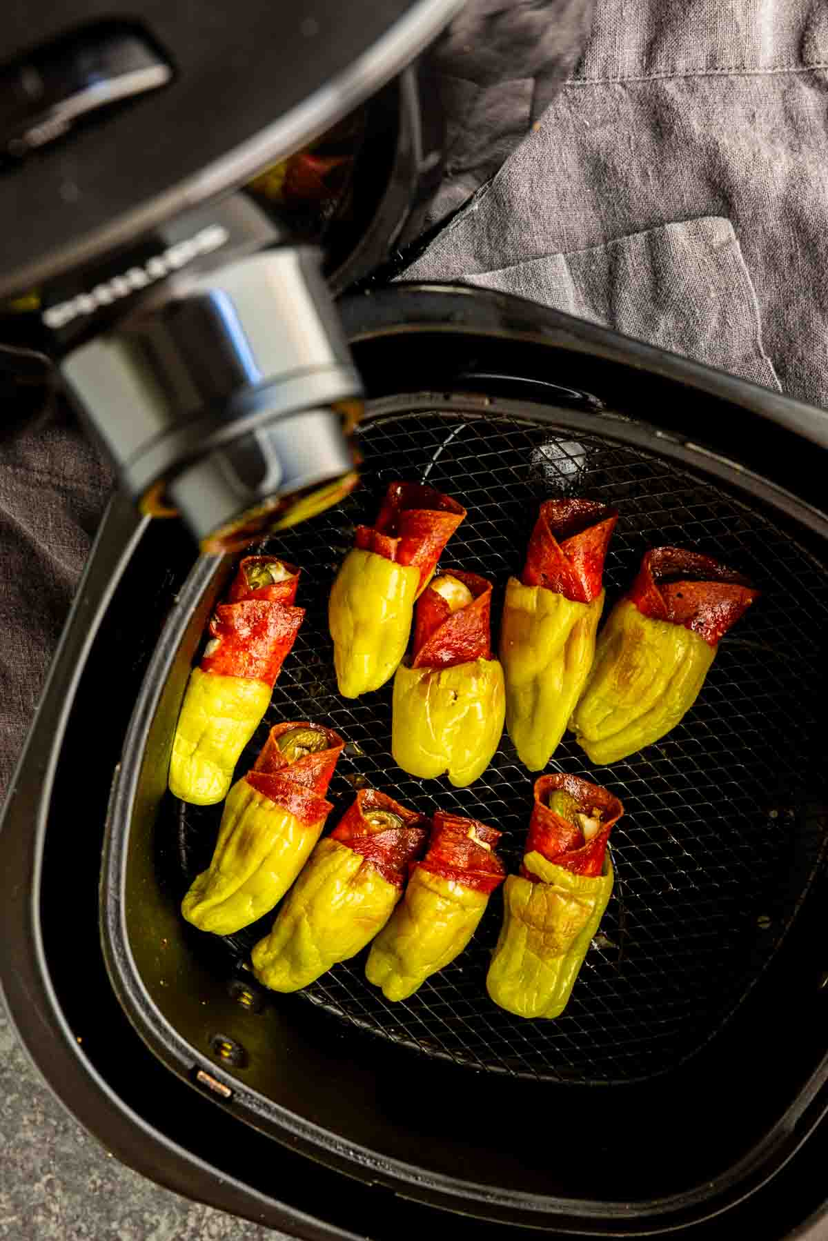 Yellow peppers wrapped in red meat slices are arranged in an air fryer basket, ready to become delicious air fryer stuffed pepperoncinis for a quick and tasty treat.