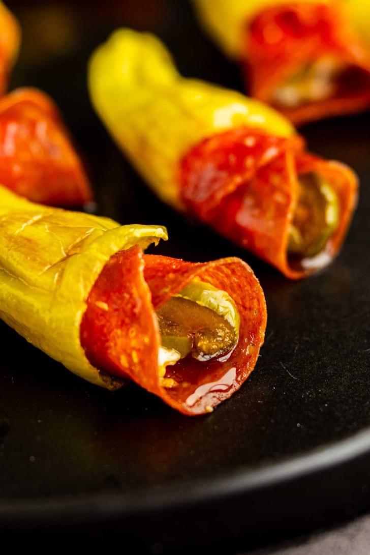 Close-up of yellow pepper slices stuffed with pepperoni and melted cheese on a black plate, reminiscent of flavorful stuffed pepperoncinis.