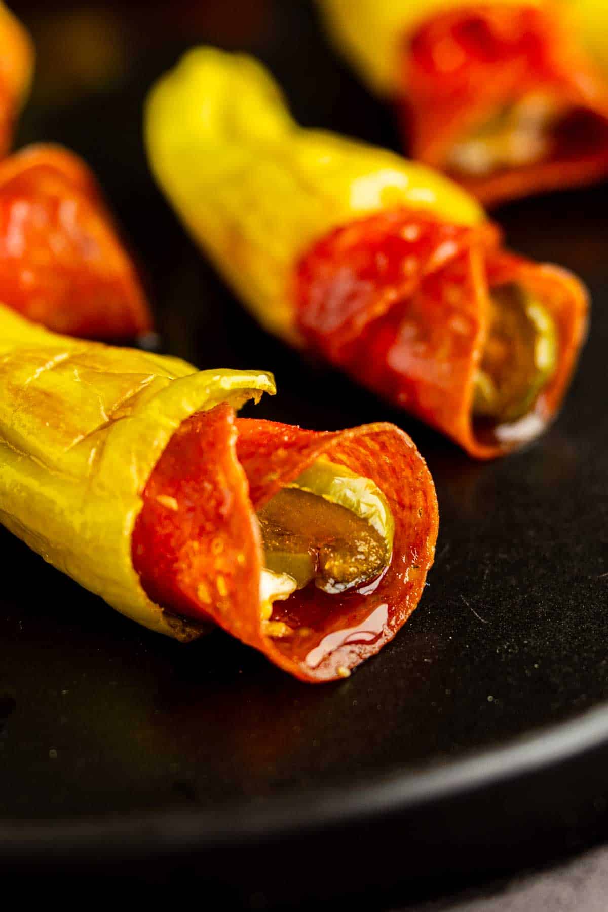 Close-up of yellow pepper slices stuffed with pepperoni and melted cheese on a black plate, reminiscent of flavorful stuffed pepperoncinis.