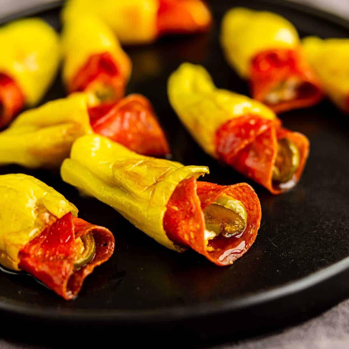 Close-up of pepperoni stuffed pepperoncinis on a black plate, showcasing these flavorful pepperoncini poppers filled with spicy slices.