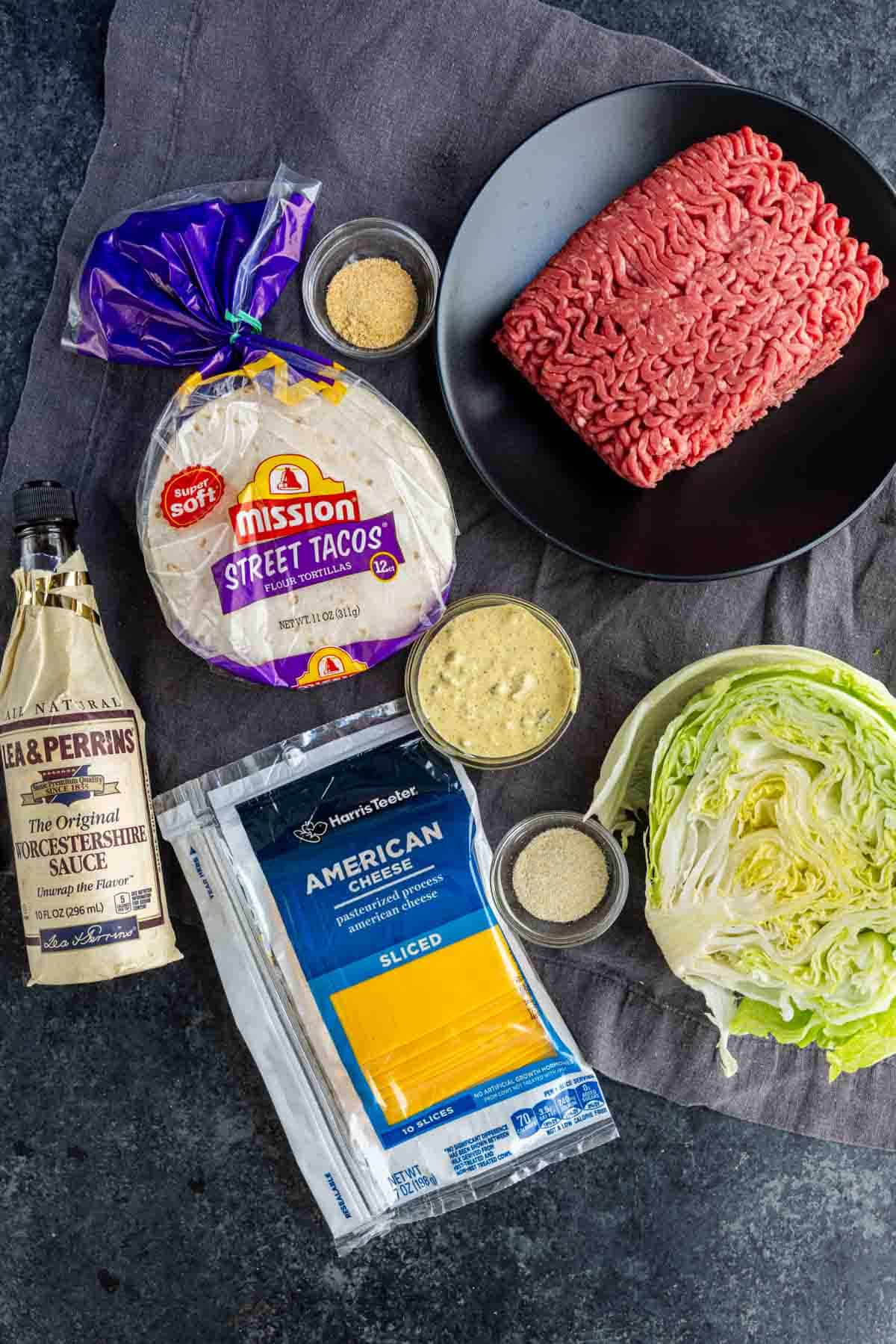 Ingredients for viral taco recipe displayed: ground beef, taco seasoning, Worcestershire sauce, street taco flour tortillas, American cheese slices, shredded lettuce, garlic powder, onion powder, and mustard—everything you need for easy weeknight dinner Big Mac smashed tacos.