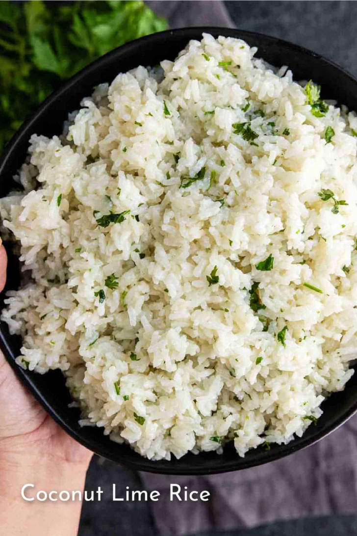 A hand holds a black bowl filled with coconut lime rice, garnished with chopped herbs. The words "Coconut Lime Rice" appear at the bottom left.
