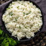 A black bowl of white rice with chopped green herbs.