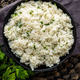 A black bowl of white rice with chopped green herbs.