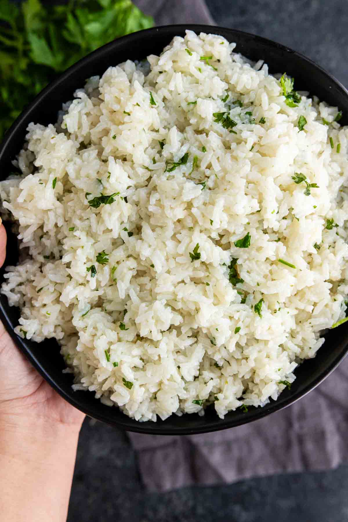 A bowl of easy coconut lime rice garnished with chopped herbs, held in one hand over a dark surface.