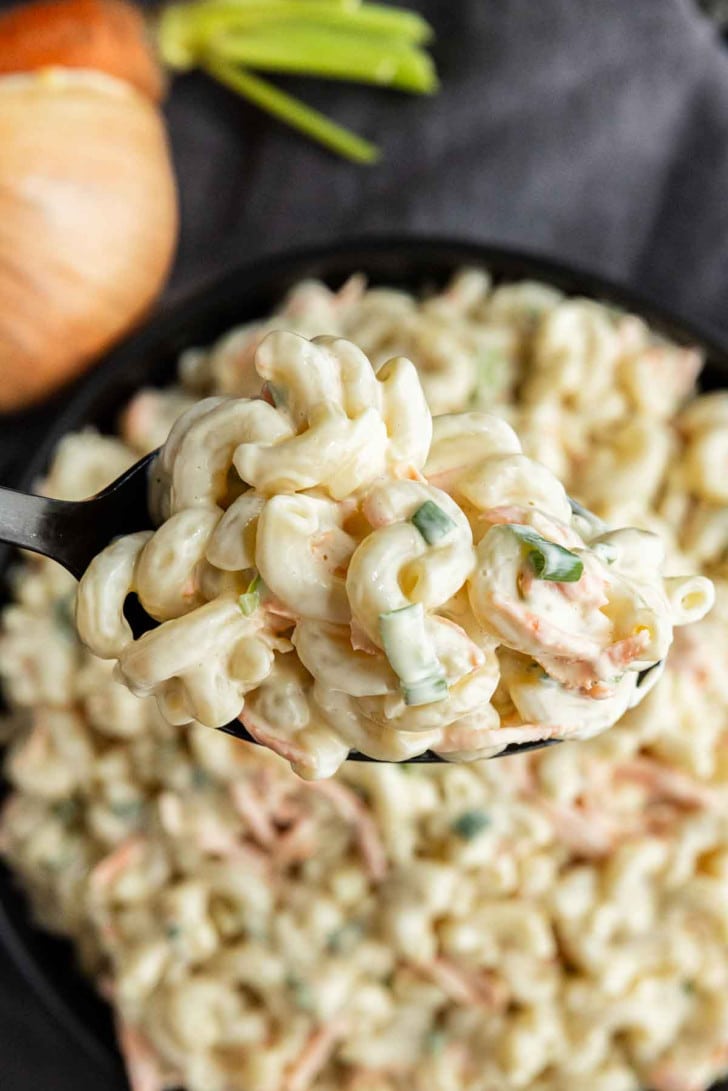 A spoonful of creamy macaroni salad with chopped vegetables held above a bowl of the same salad.