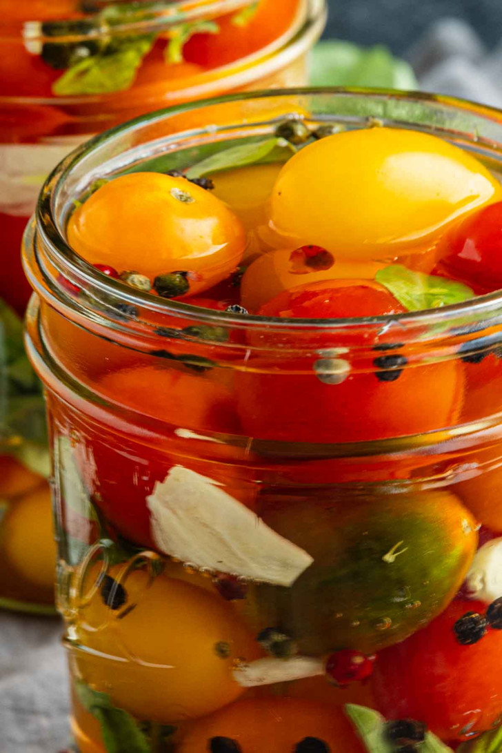 Close-up of a glass jar filled with colorful cherry tomatoes, herbs, peppercorns, and slices of garlic in brine—a delicious example of how to pickle cherry tomatoes for a vibrant quick pickle recipe.
