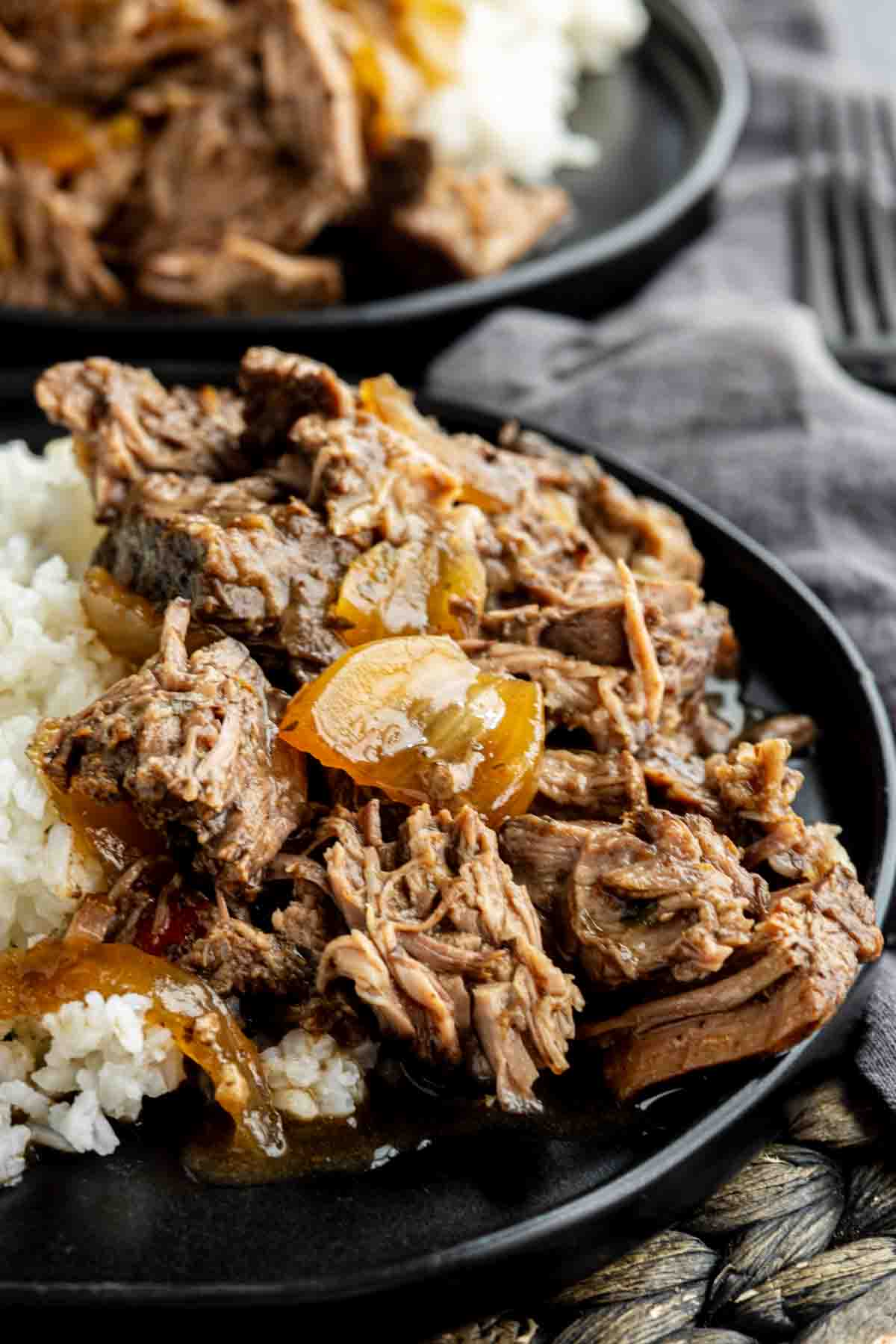 Shredded beef with cooked onions, reminiscent of a Slow Cooker Georgia Pot Roast, served over white rice on a black plate.