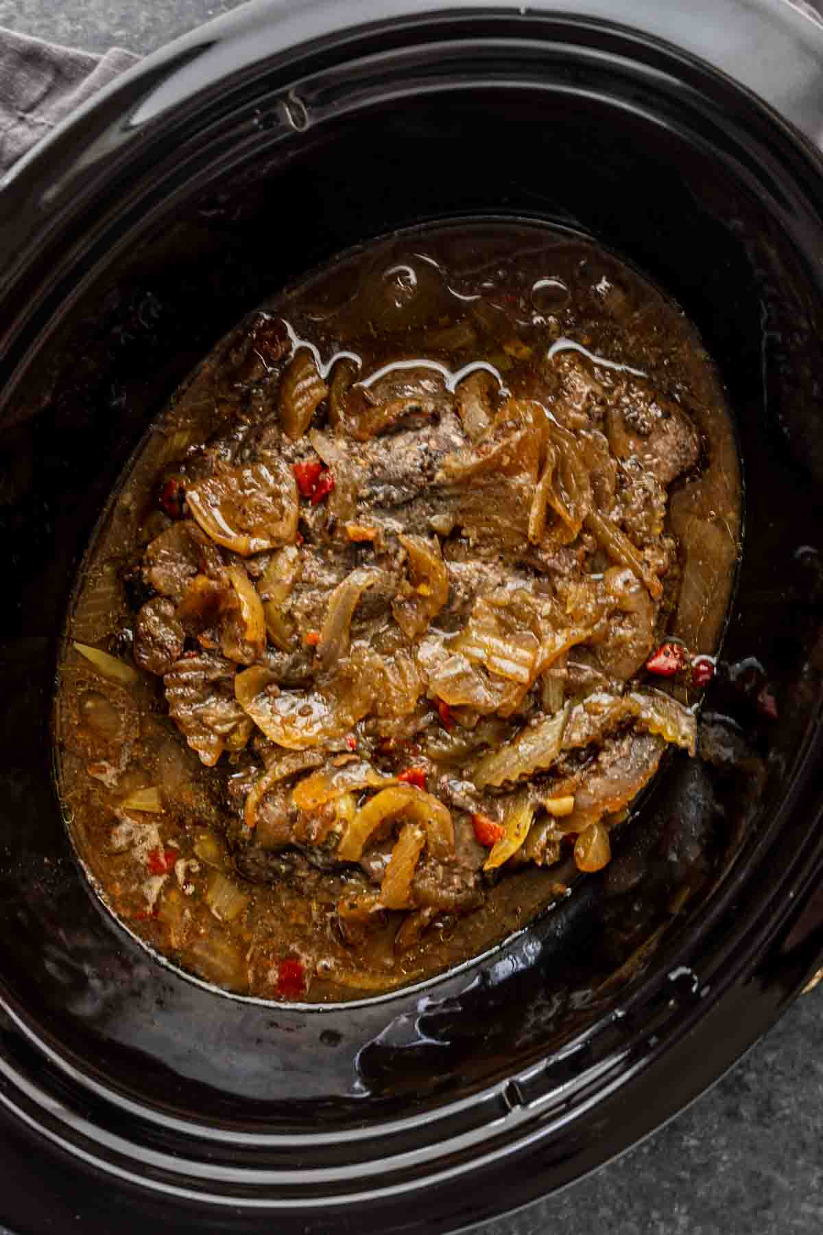 Beef and onions cooked in broth with red peppers in a black slow cooker, this easy slow cooker dinner is a classic Slow Cooker Georgia Pot Roast that’s perfect for busy weeknights.