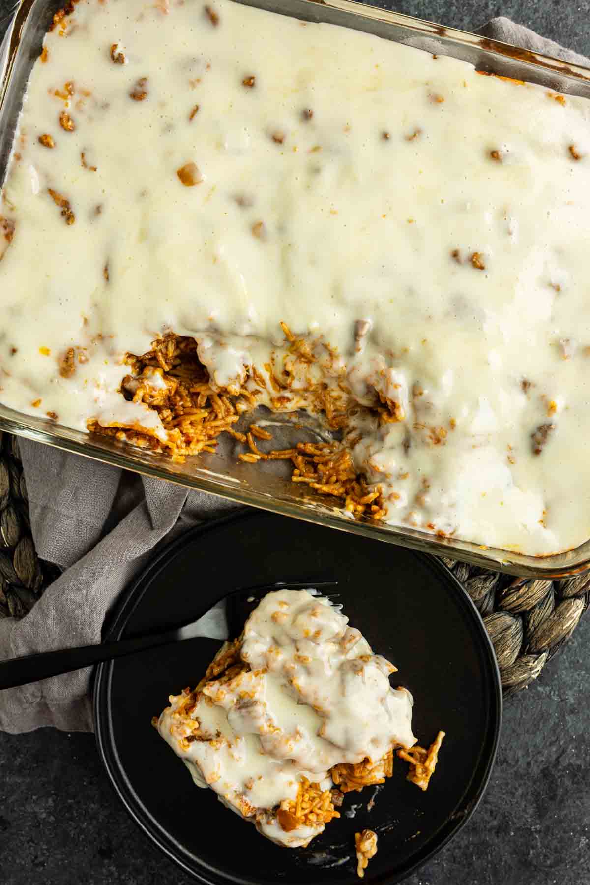 A casserole dish of creamy baked swim queso chicken and rice casserole with a portion served on a black plate, both covered in queso blanco, inspired by the viral TikTok chicken recipe.