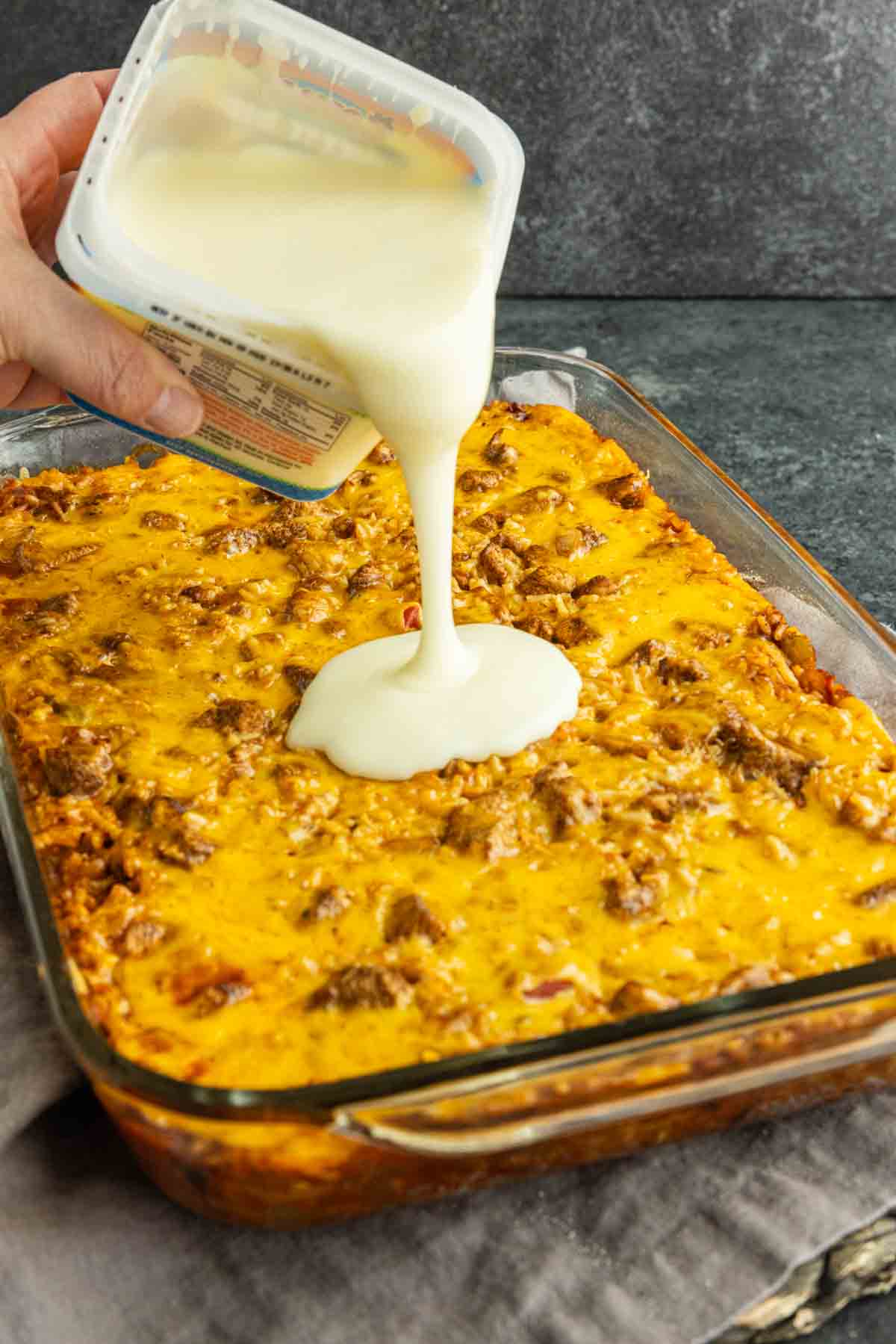 Warm queso being poured over baked chicken and Mexican rice casserole.