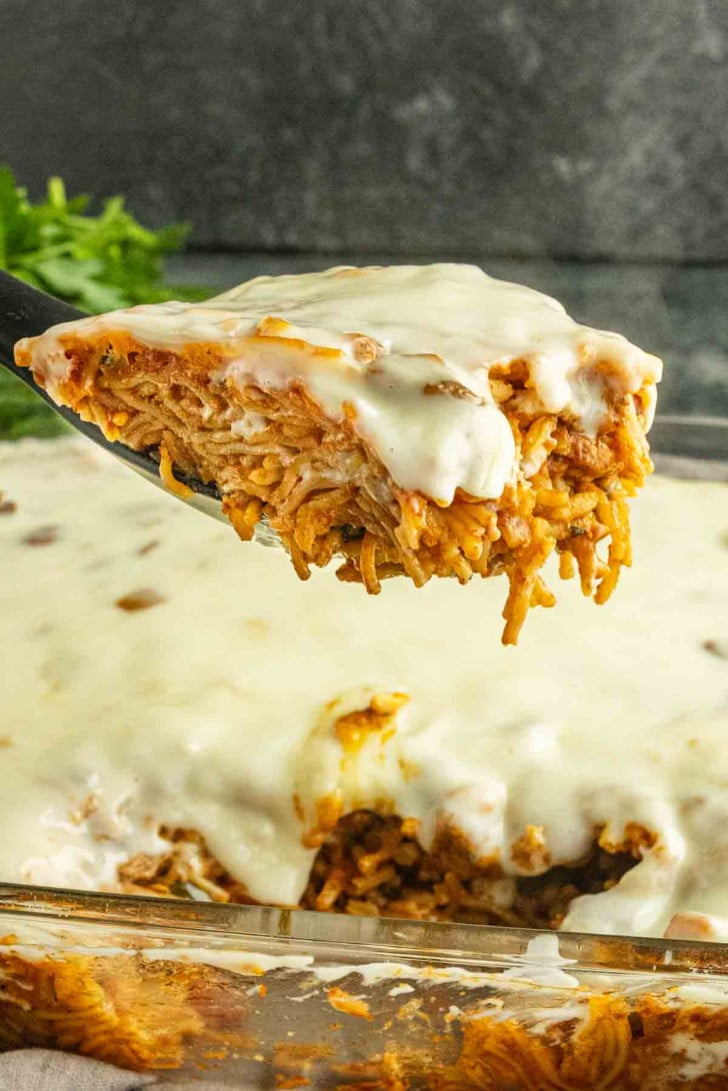 A spatula lifts a slice of baked spaghetti topped with melted cheese from a glass casserole dish, reminiscent of the crave-worthy comfort found in viral TikTok chicken recipes like swim queso chicken and rice.