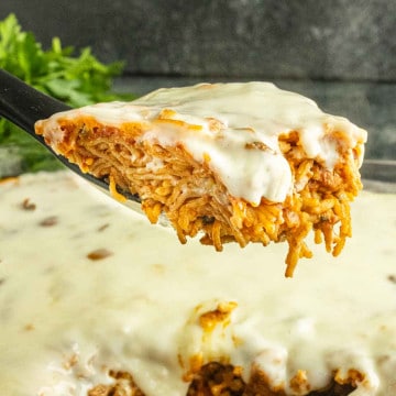 A spatula lifts a cheesy baked spaghetti slice topped with melted white cheese from a casserole dish, reminiscent of the creamy goodness found in the viral TikTok chicken recipe known as swim queso chicken.