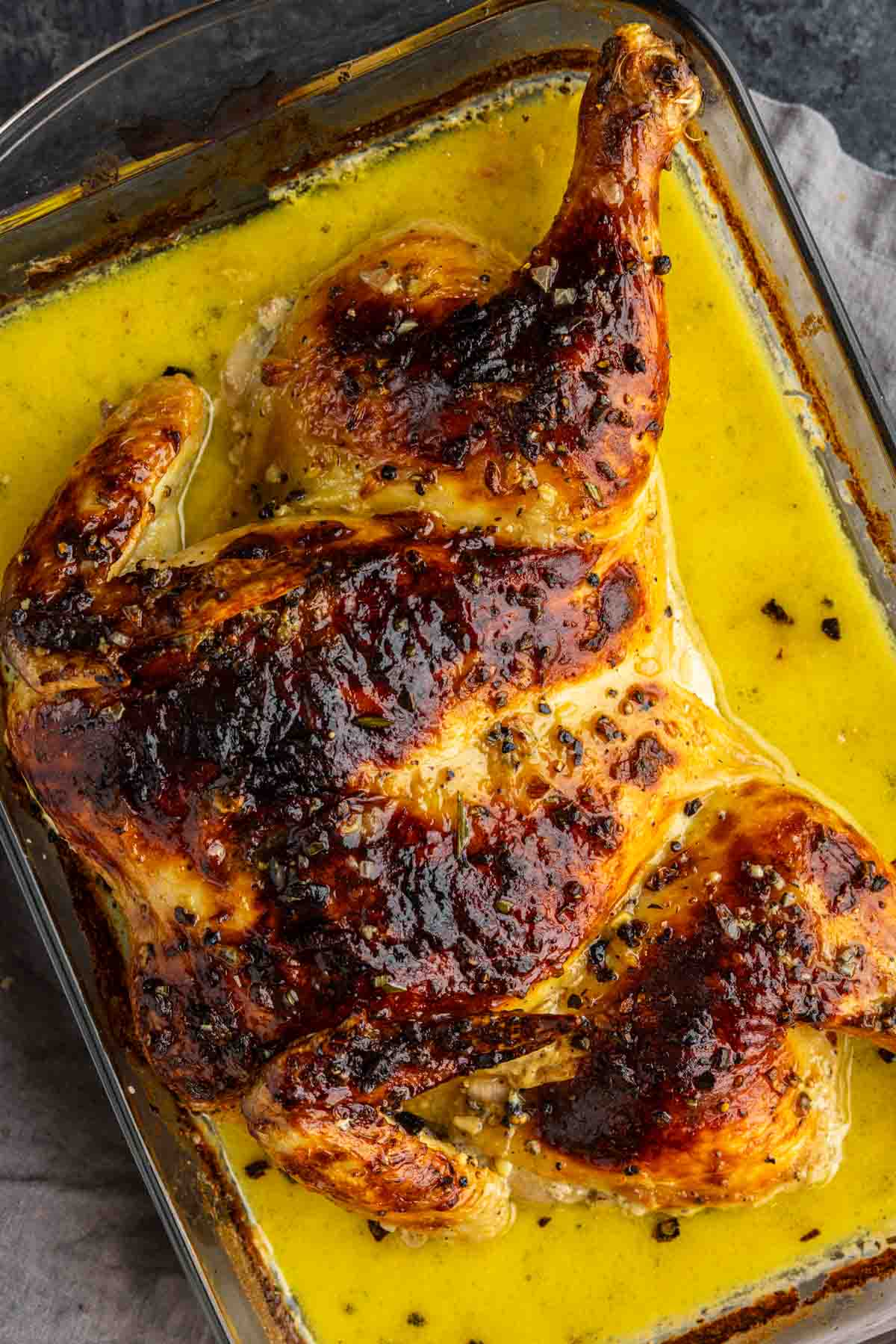 Roasted spatchcock chicken with crispy skin sits in a glass baking dish surrounded by a rich, yellow peppercorn sauce—a true French-inspired chicken reminiscent of classic Chicken Au Poivre.