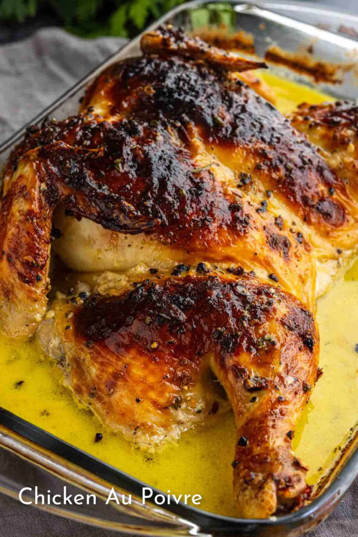 Roasted chicken with crispy, browned skin in a glass baking dish, sitting in a peppery yellow sauce. Text on image reads, “Chicken Au Poivre.”.