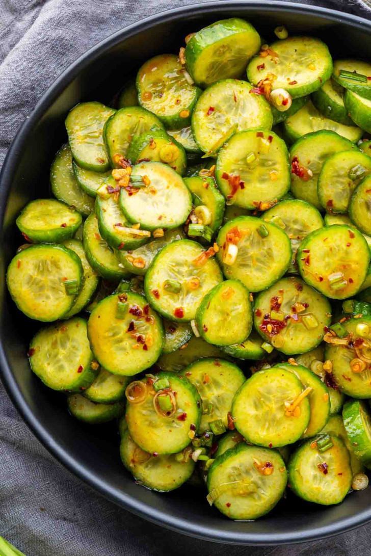 A black bowl filled with spicy cucumber salad seasoned with green onions and chili crisp.