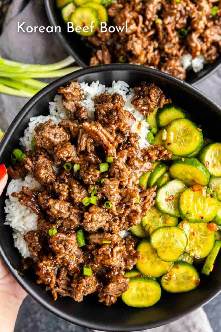 A black bowl with white rice, cooked ground beef in sauce, and sliced cucumbers, garnished with chopped green onions.