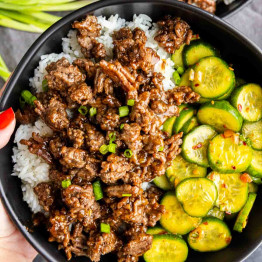 Bowl with white rice, ground beef in sauce, sliced cucumbers, and chopped green onions.