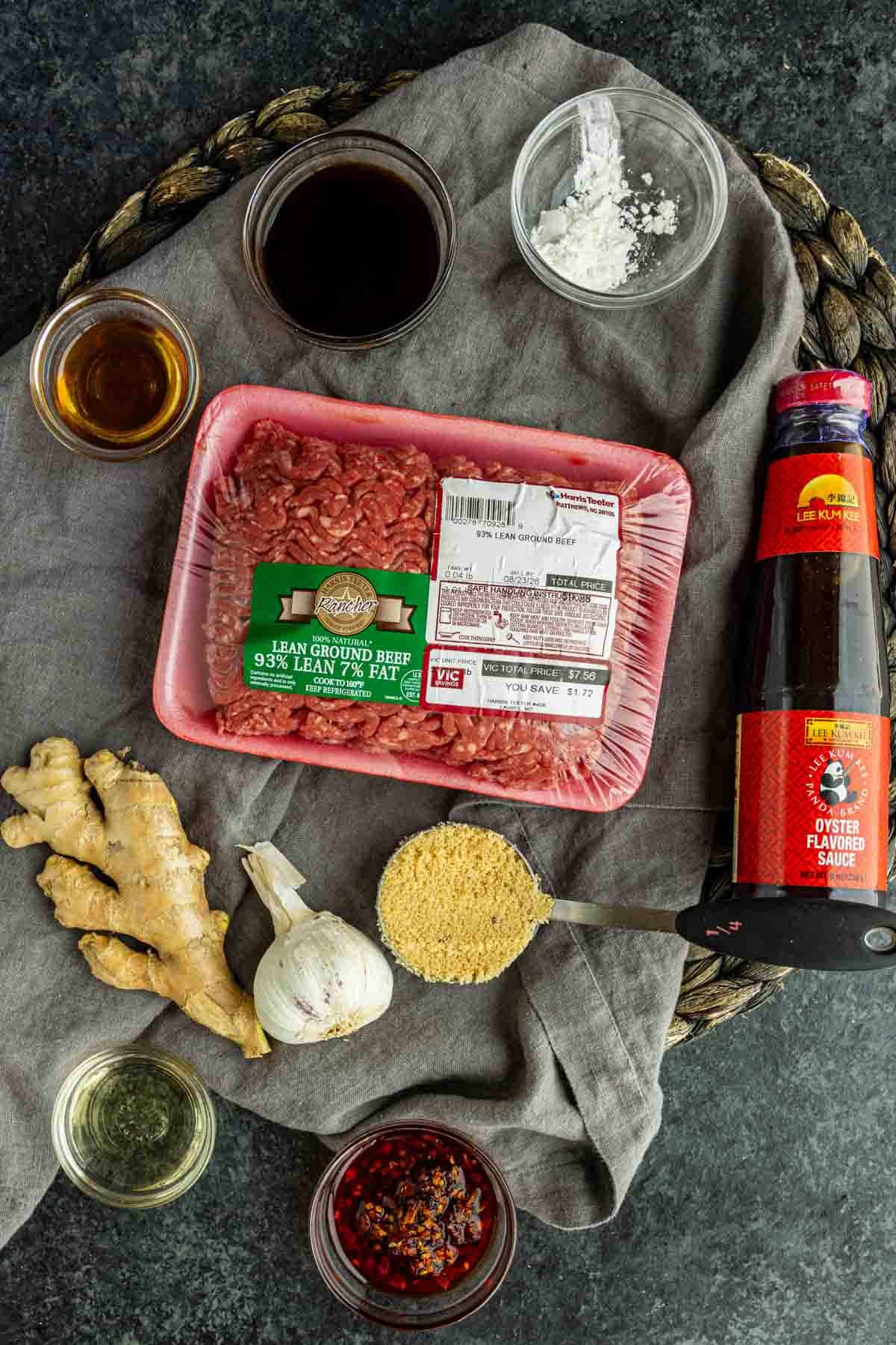 A package of lean ground beef surrounded by oyster sauce, ginger, garlic, chili crisp, bouillon, and liquid ingredients for a Korean beef and rice bowl.