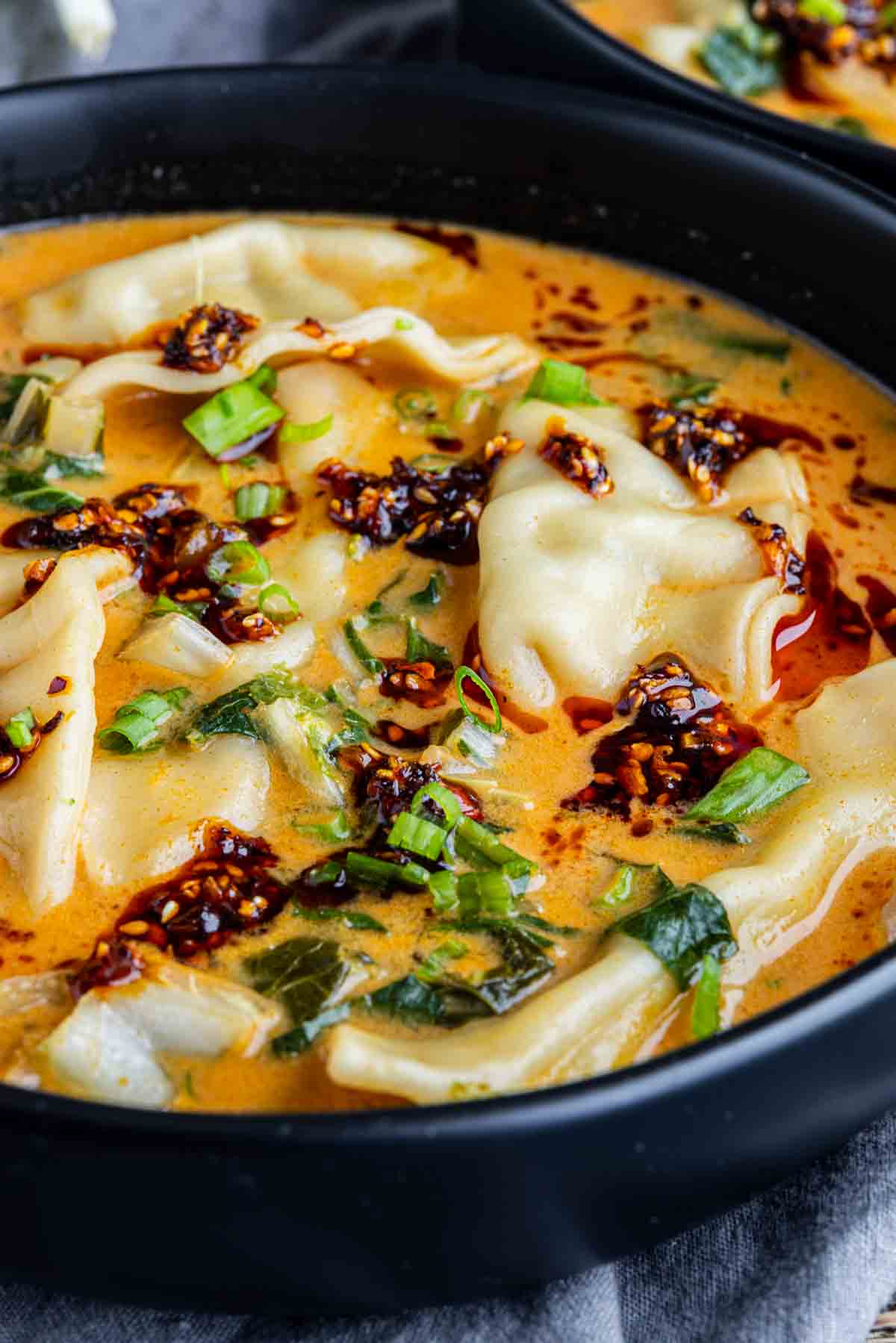 A bowl of dumplings in a creamy, orange-colored broth, topped with chili oil and chopped green onions—this viral dumpling soup features rich coconut curry flavors that make every bite irresistible.