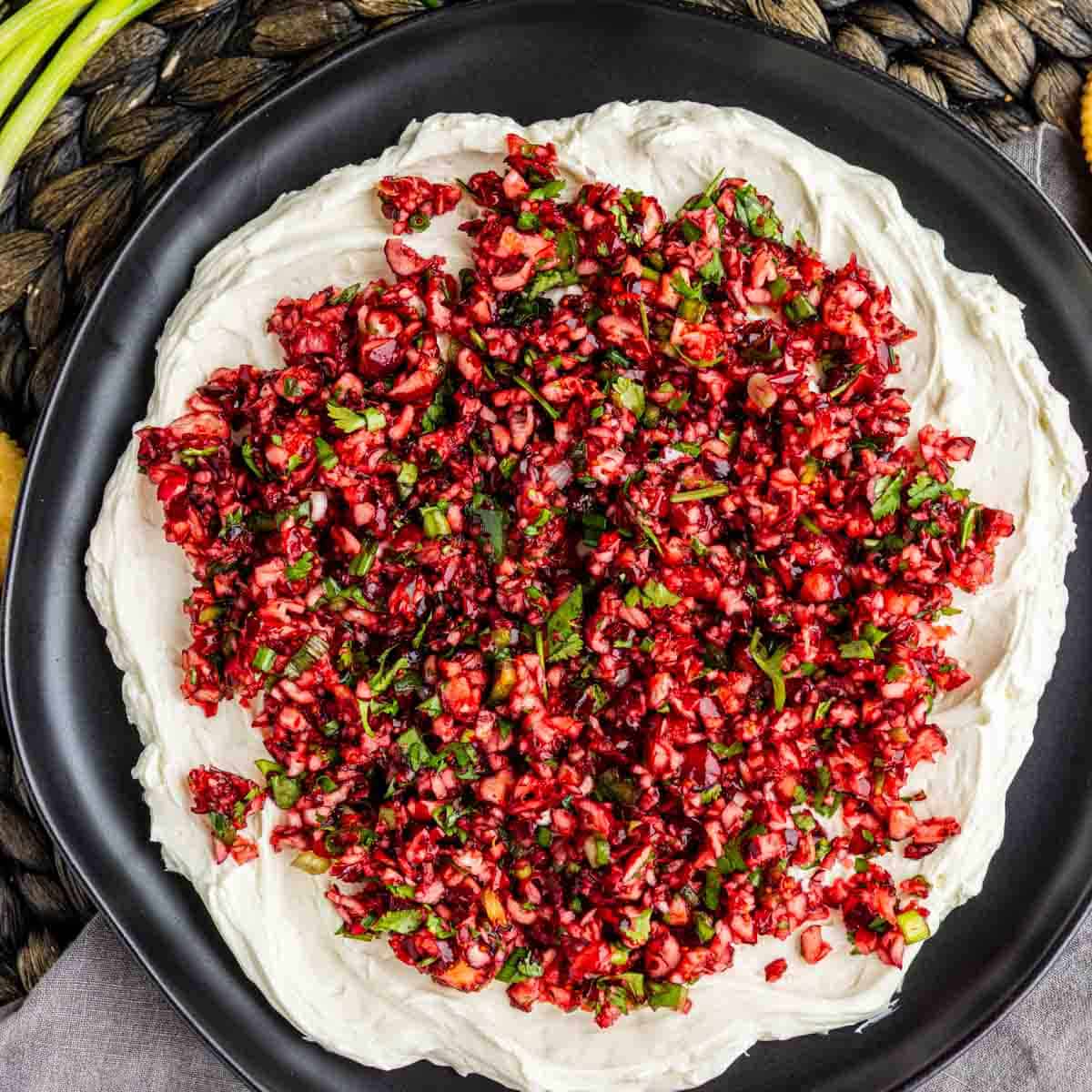 A layer of creamy cranberry jalapeño dip topped with a chopped cranberry and herb salsa on a black plate.