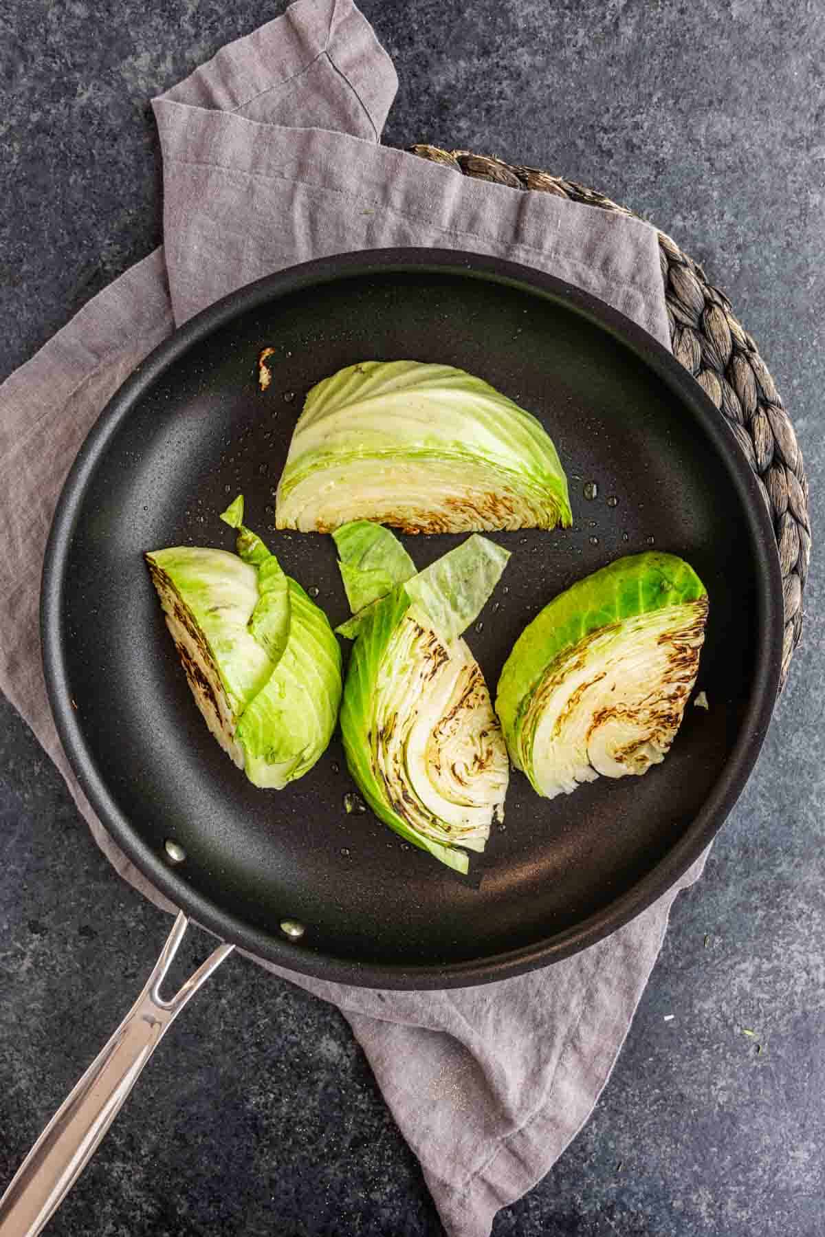 Four wedges of garlic butter melting cabbage searing in a black skillet.