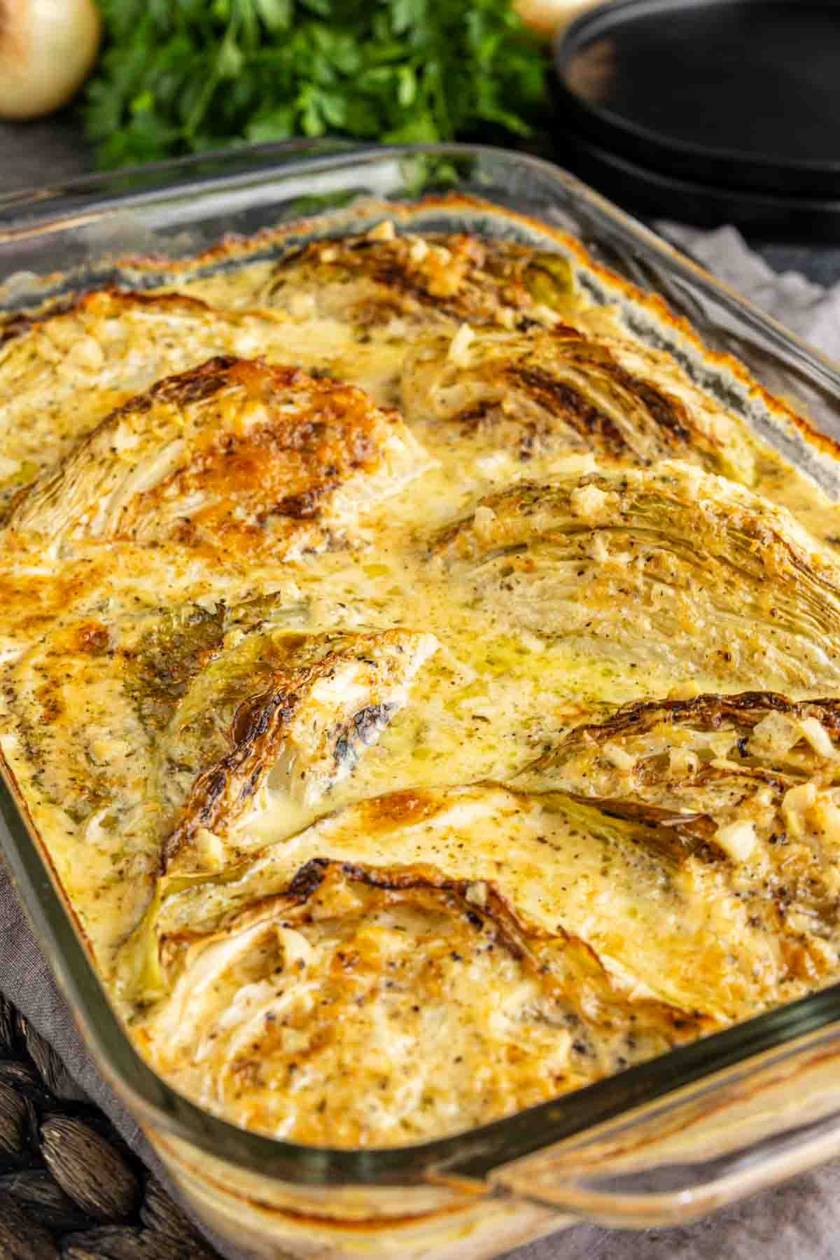 Roasted garlic butter melting cabbage wedges in a creamy sauce in a glass baking dish.