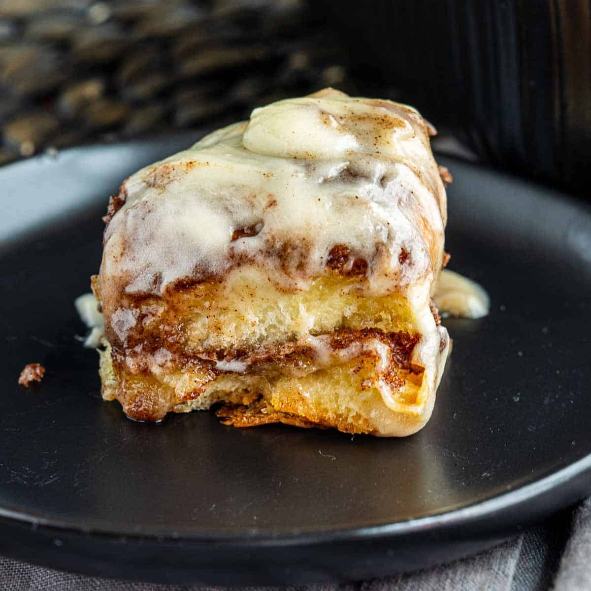 A King’s Hawaiian cinnamon roll with icing on a black plate.
