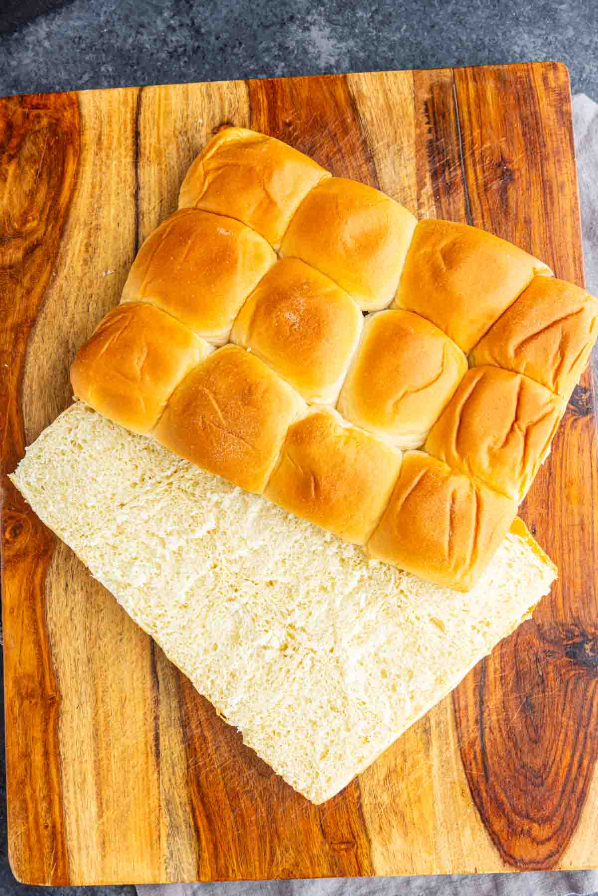 A sheet of golden-brown King’s Hawaiian cinnamon rolls sliced in half on a wooden cutting board.