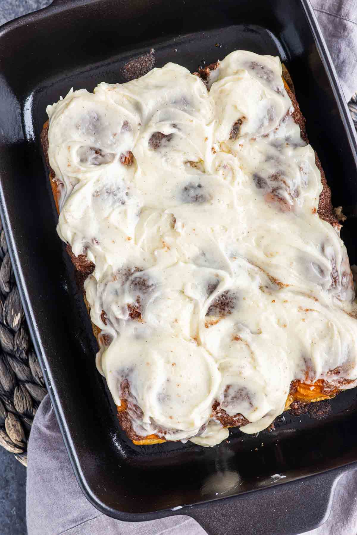 A rectangular baking dish filled with King’s Hawaiian cinnamon rolls topped with a thick layer of white frosting.
