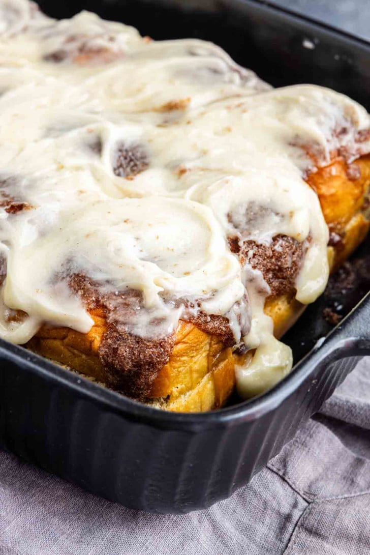 Cinnamon rolls with white icing in a black baking dish.