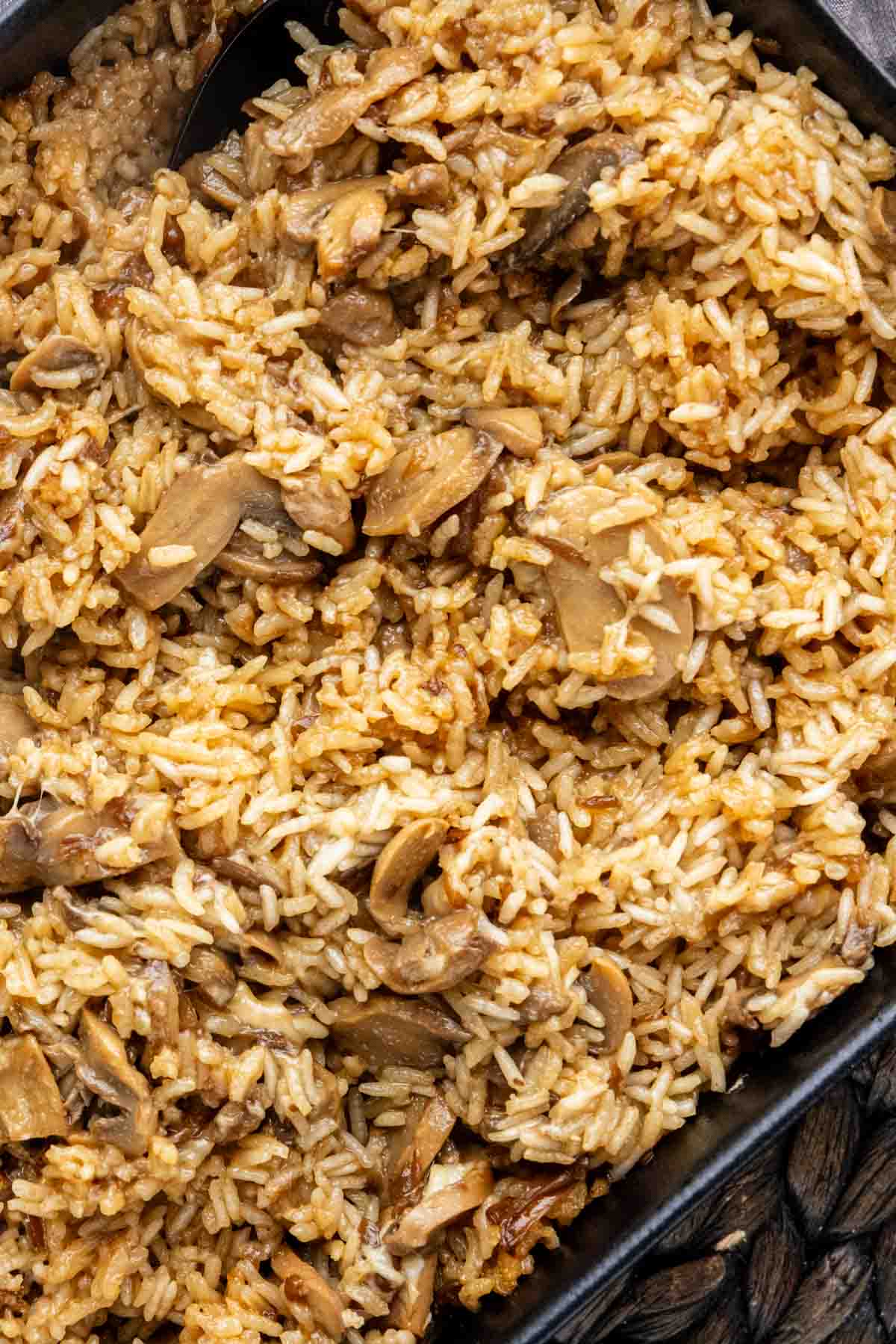 A black spoon stirs a pan of French onion butter rice with mushrooms.
