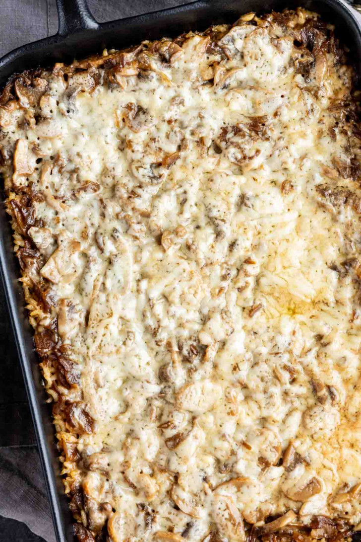 Baked mushroom and rice casserole with a rich French onion butter sauce, topped with melted cheese in a cast iron skillet.
