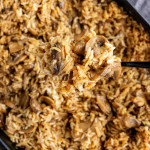 A spoonful of French onion butter rice casserole being lifted from a baking dish.