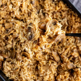 A spoonful of French onion butter rice casserole being lifted from a baking dish.