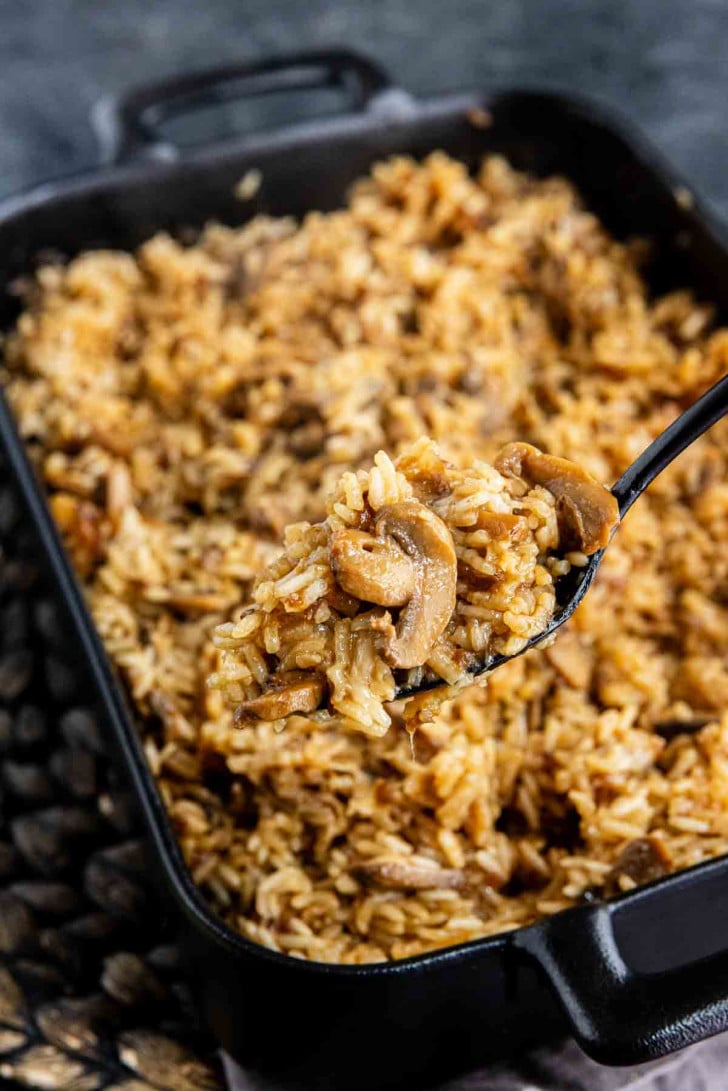 A spoonful of mushroom rice being lifted from a baking dish filled with the same dish.