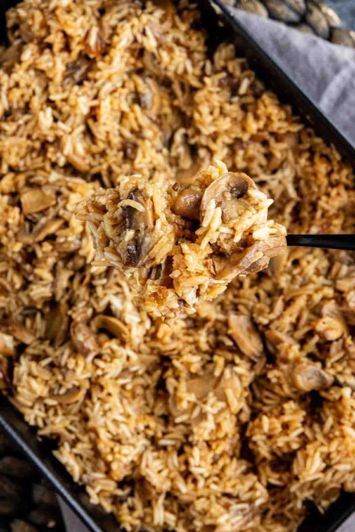 A spoonful of mushroom rice casserole being lifted from a baking dish.