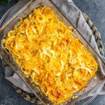 Baked potato and sweet onion casserole topped with melted cheese in a glass baking dish.