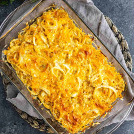 Baked potato and sweet onion casserole topped with melted cheese in a glass baking dish.